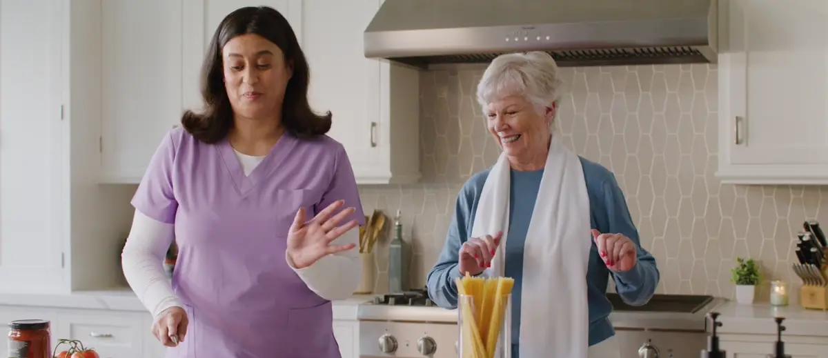 A caregiver and an older woman enjoying cooking together